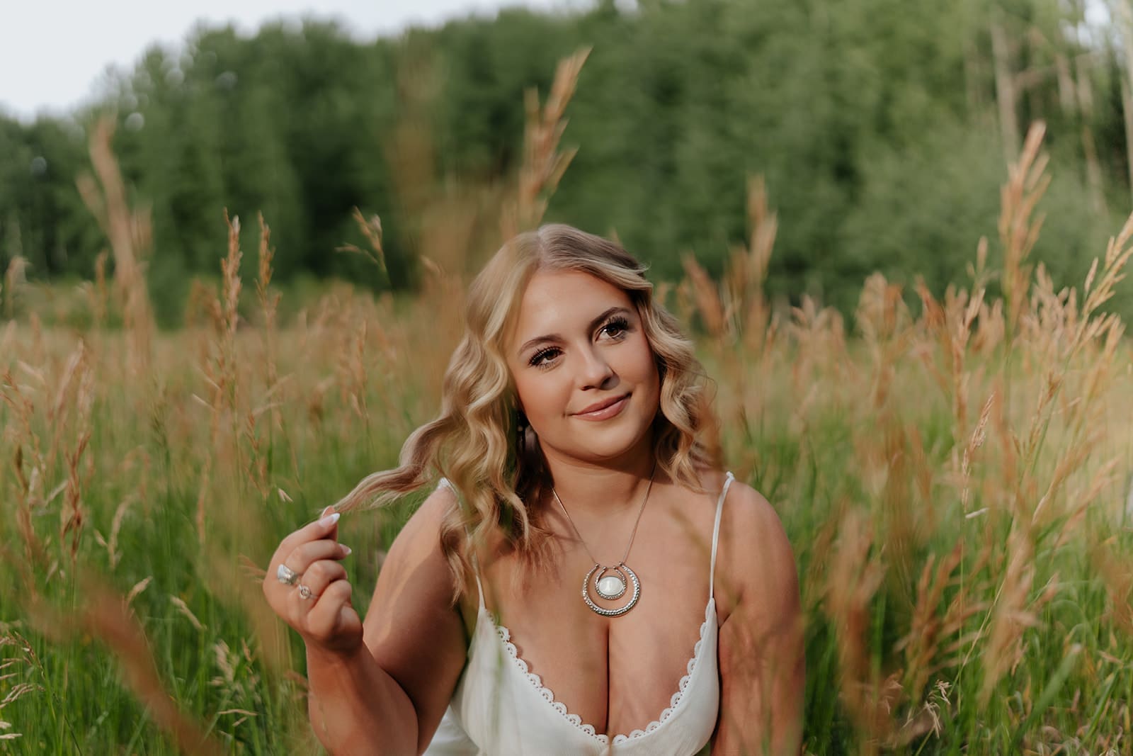Senior girl smiling and playing with her hair in a field in southwestern Colorado