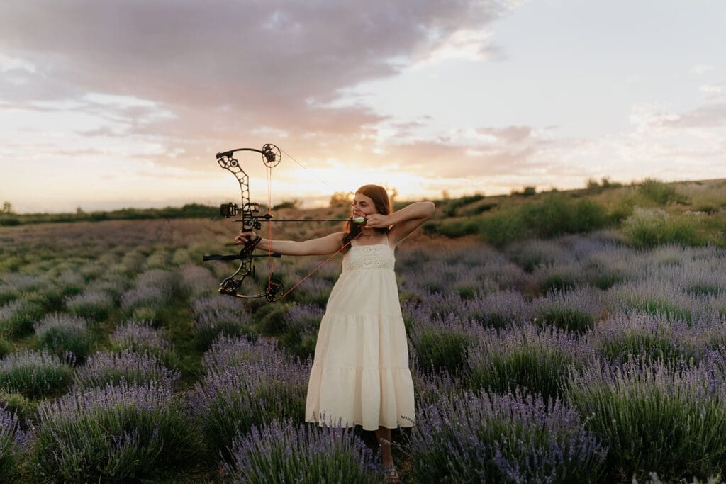 High school senior standing confidently in a lavender farm with her bow and arrow, blending strength and softness